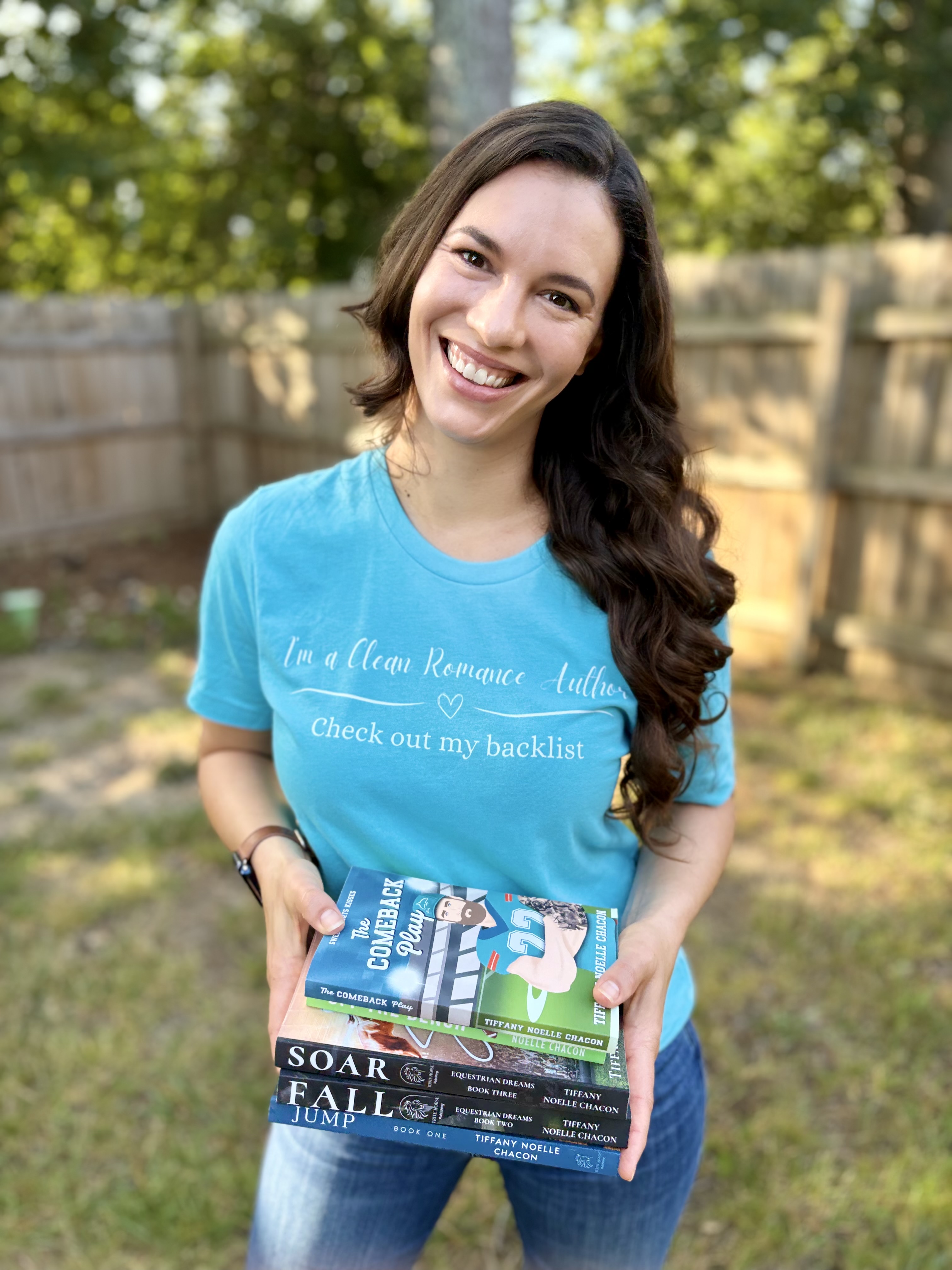 Tiffany Noelle Chacon smiling outdoors, holding a stack of her novels